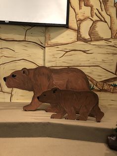 two brown bears standing in front of a screen with trees and rocks painted on it