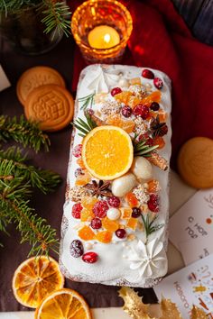 a cake with oranges, cranberries and pine cones on it next to some cookies