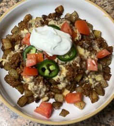 a white plate topped with potatoes covered in cheese and toppings next to a green pepper