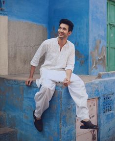 a man sitting on the side of a blue building