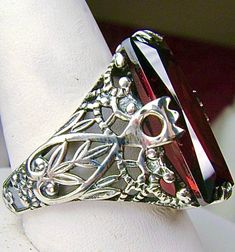 Garnet CZ Sterling Silver RingIntaglio Design#D31 This sterling silver ring is a reproduction of a Victorian filigree antique ring. Inspired by the intricate Victorian designs of the late 1800s and turn of the century, this gorgeous ring is offered in sterling silver. The lovely ring is set with a flawless 7ct Garnet CZ (cubic zirconia) gemstone, by your choice. The baguette shape gemstone is 18mm long by 9mm wide. The ring is 8mm off the finger. The inside of the band is marked 925 for sterling silver. This ring has beautiful sterling silver filigree detail. The gem is held in place with the prongs that reach up from the filigree. There are small petals that climb up either side of the gem, and the details travel all down the band. This ring is a fanciful example of vintage style. Brillia Silver Baguette Cut Crystal Ring For Gift, Formal Garnet Jewelry With Stone Setting, Silver Garnet Wedding Jewelry, Silver Garnet Crystal Ring For Wedding, Wedding Jewelry With Garnet Filigree, Wedding Jewelry With Filigree Garnet, Elegant Oval Crafted Jewelry, Ornate Diamond-cut Ring Jewelry, Ornate Diamond Cut Ring Jewelry