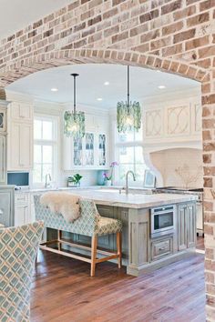 an open kitchen and living room area with brickwork on the walls, hardwood flooring and white cabinets