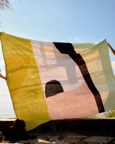 two people holding up a large quilt on the beach