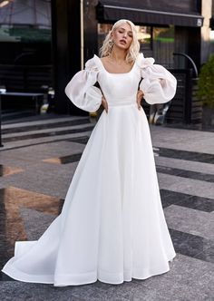 a woman in a white wedding dress standing on the street with her hands on her hips