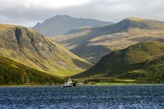 there is a boat that is in the water and mountains are behind it, but not far from the shore