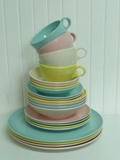 stack of multicolored cups and saucers sitting on top of each other in front of a white wall