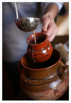 a person is pouring something into a small vase with a spoon in it and another hand holding the bowl