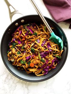 a pan filled with noodles and vegetables on top of a table next to a fork