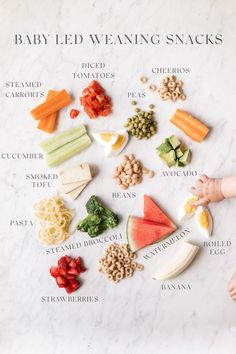 baby's hand reaching for an assortment of baby led weaning snacks on a marble surface