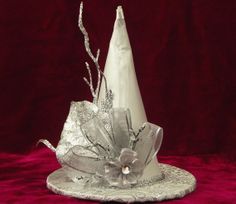 a white hat with silver ribbons and flowers on it, sitting on a red velvet surface