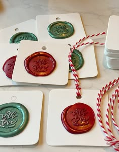 four waxed christmas ornaments with red and green twine on white tags next to candy canes