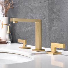 modern bathroom faucet with two handles and gold fixtures on the countertop in front of a gray marble wall