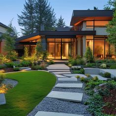 a modern house is lit up at night with lights on the windows and grass in front