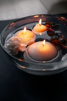 three lit candles floating in water on a table