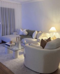 a living room filled with white furniture and pillows on top of a rug next to a glass coffee table