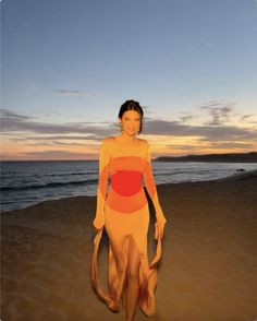 a woman sitting on top of a sandy beach next to the ocean at sunset or dawn