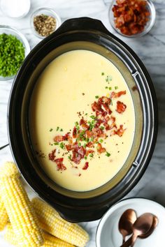 a crock pot filled with potato soup next to corn and other dishes on the table