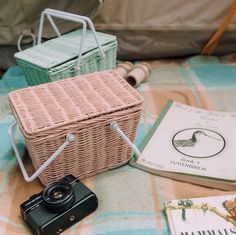 a camera and some books on a bed next to a wicker basket with handles