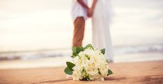 a bride and groom standing on the beach with their wedding bouquet in front of them