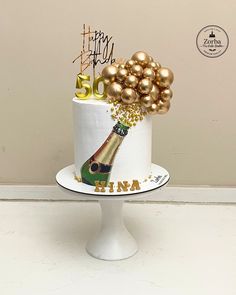 a birthday cake with champagne and gold balloons on the top is sitting on a pedestal