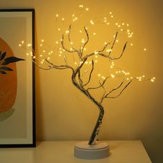 a lighted tree is sitting on a table next to a framed photograph and an orange wall