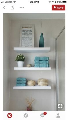 a bathroom with white shelves and blue towels on top of the shelf above the toilet