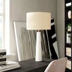 a white lamp sitting on top of a table next to a book shelf and chair