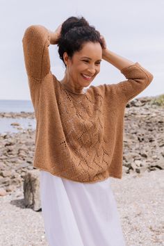 a woman standing on top of a beach next to the ocean wearing a brown sweater