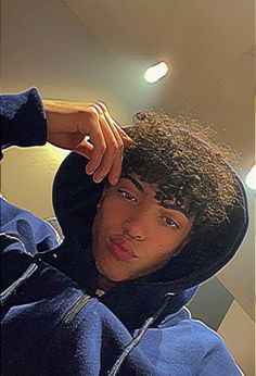 a young man with curly hair wearing a blue hoodie and looking at the camera