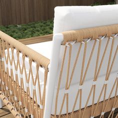 a wicker bed with white sheets and pillows on top of wooden floor next to fence