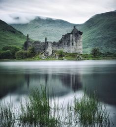 a castle sitting on top of a lush green hillside next to a lake and mountains