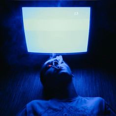 a man laying down in front of a computer monitor with the screen lit up blue