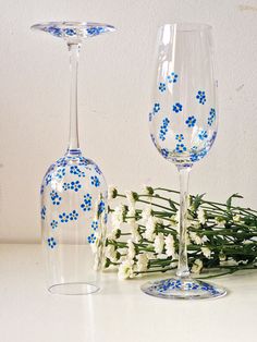 two wine glasses sitting next to each other on a white table with flowers in the background