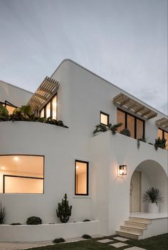 a white house with lots of windows and plants on the side of it at dusk