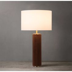 a table lamp with a white shade on it and a wooden base in front of a gray wall