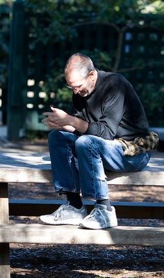 a man sitting on a park bench looking at his cell phone while he sits down