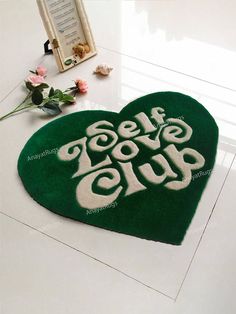 a green heart shaped rug with the words self love club on it next to flowers