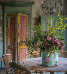 a vase with flowers on top of a table next to chairs and a chandelier