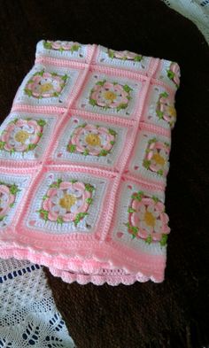 a pink crocheted blanket sitting on top of a table next to a doily