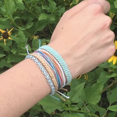 a woman's arm with several bracelets on it and flowers in the background