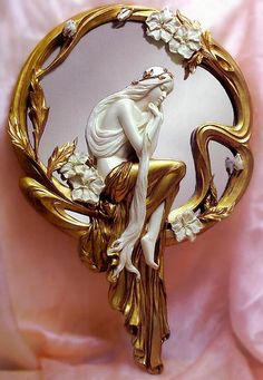 a white and gold brooch with a woman sitting on it's back holding flowers