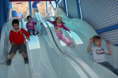 three children sliding down a slide in a play area