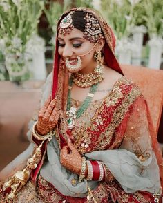 a woman in a red and grey bridal outfit with jewelry on her face, smiling at the camera