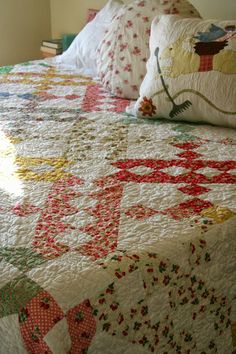 a bed with a quilt and pillows on it in a room next to a window