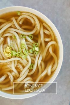 a white bowl filled with noodles and broth sitting on top of a gray table