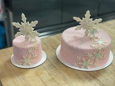 two frosted cakes with snowflakes on them sitting on top of a wooden table