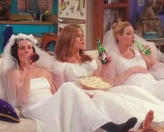 three women in wedding dresses sitting on a couch and one is holding a bottle of beer