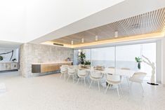 a dining room with white chairs and a table in the foreground is an open kitchen