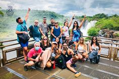 a group of people standing on top of a wooden bridge next to a river and waterfall