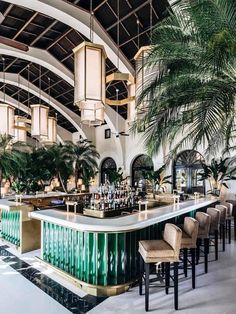 an indoor bar with palm trees in the background and hanging lights on the ceiling above it